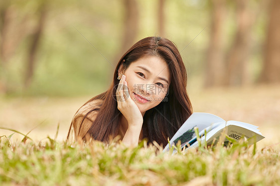 年轻女性趴在草地上看书图片