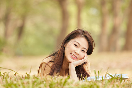 年轻女性趴在草地上看书图片