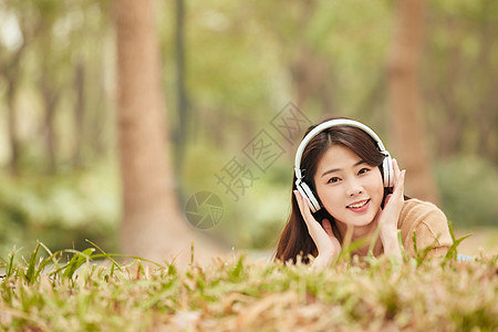 年轻女性趴在草地听音乐图片