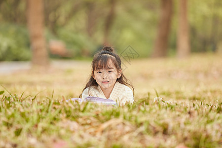 小女孩趴在草地上读书图片