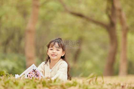 小女孩趴在草地上看童话故事图片