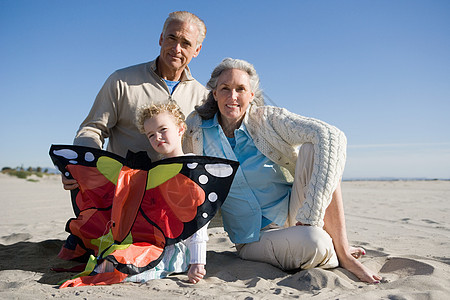 祖父母和孙女坐在沙滩上拿风筝背景图片