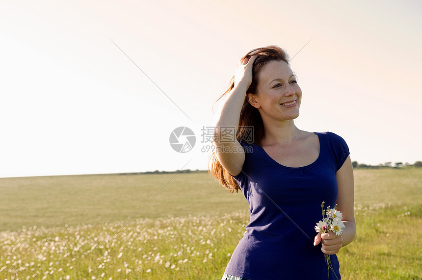 微笑的女人在草地上拿着花图片
