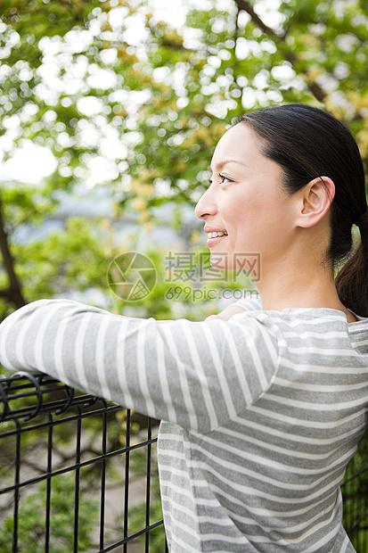 日本妇女靠在树边的栅栏上图片