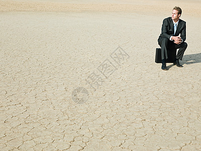 商人坐在沙漠里的公文包上图片