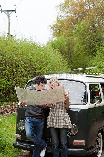 年轻夫妇坐在露营车旁看地图图片