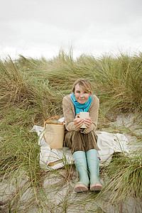 坐在沙丘上喝热饮料的女人图片