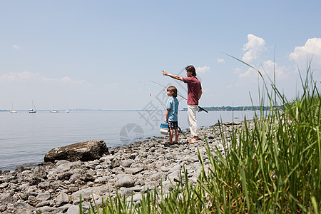 父亲和儿子带着鱼竿在海滩上图片