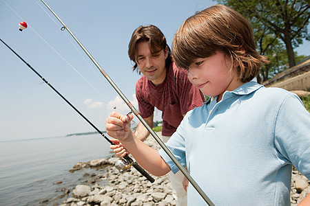 父亲和儿子带着鱼竿在海滩上图片