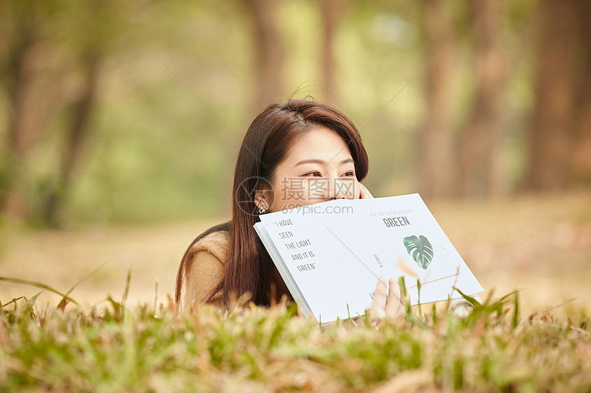 年轻女性趴在草地上看书图片