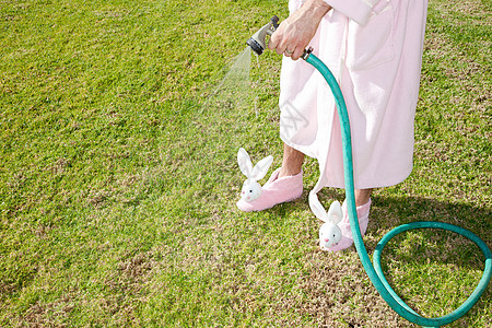 穿着粉红色长袍和兔子拖鞋的男人在浇灌草坪图片
