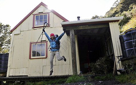 新西兰塔拉鲁纳山脊，女徒步旅行者在屋外半空中跳跃图片