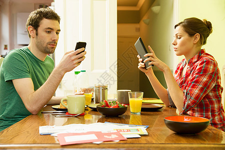 男人使用智能手机,女人在早餐使用数字平板电脑图片