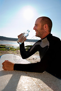 坐在冲浪板旁的男人微笑着喝水图片