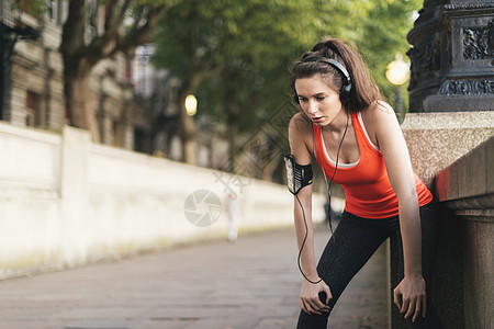 女跑步者戴着耳机在河边休息背景图片