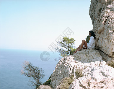 坐在海边大石头上的女人图片