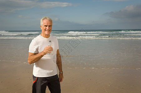 男性拿着饮用水在海滩上图片