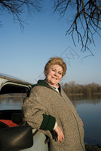 老妇人靠在河边的车上图片