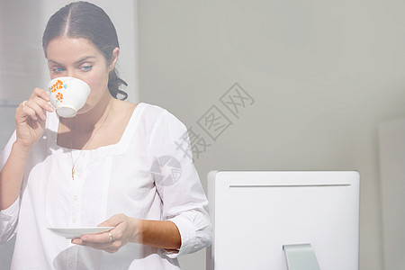 女人在电脑桌上喝茶图片
