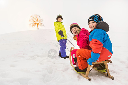 在雪地里拉着两个朋友的男孩图片