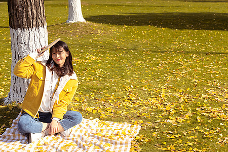 坐在铺满银杏叶的毯子上手拿书本的女孩背景图片
