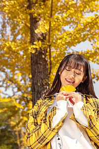 金色银杏叶银杏树下手捧银杏叶的女孩背景