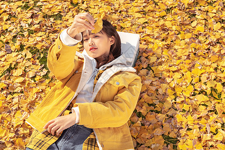 躺在铺满银杏叶草坪上的甜美女孩图片