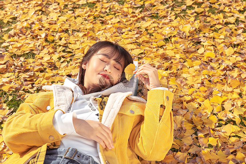 躺在铺满银杏叶草坪上的甜美女孩图片