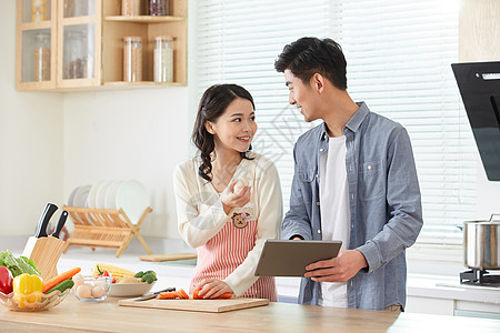 年轻夫妻拿着平板电脑学习做菜高清图片