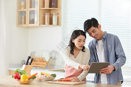 年轻夫妻拿着平板电脑学习做菜高清图片