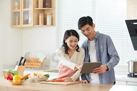 年轻夫妻拿着平板电脑学习做菜高清图片