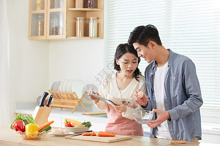 初中学年轻夫妻拿着平板电脑学习做菜背景