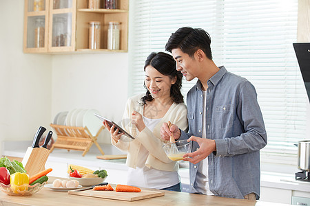 年轻夫妻拿着平板电脑学习做菜高清图片