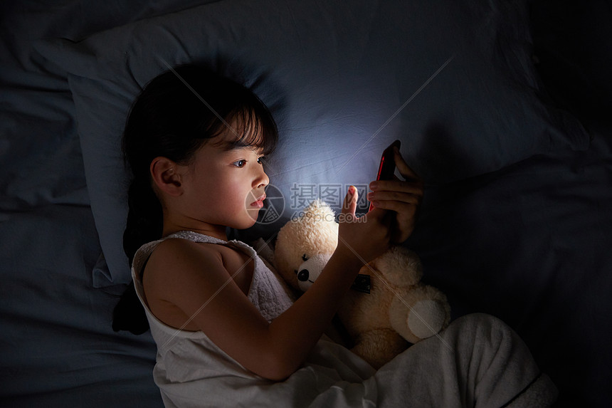 小女孩躺在床上玩手机图片