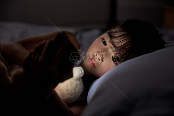 小女孩夜晚躺床上玩手机图片