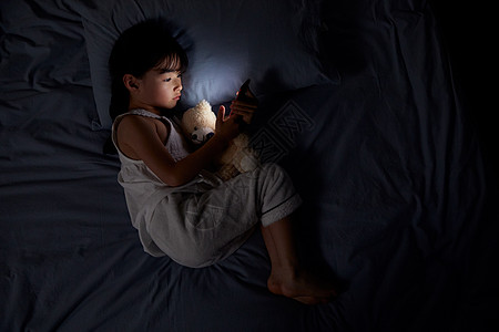 玩手机的女生小女孩夜晚躺床上玩手机背景