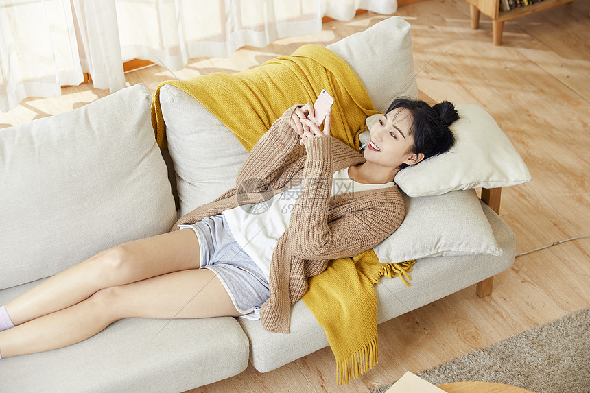年轻美女躺在沙发上玩手机