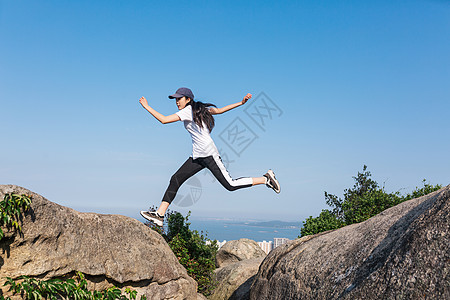 人山顶郊外石头上跳跃中的美女背景