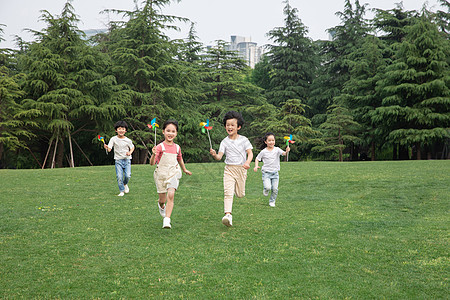 在草地上在户外手举风车奔跑的小朋友们背景