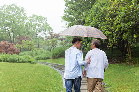 爸爸和儿子中老年父子下雨天撑伞逛公园背影背景