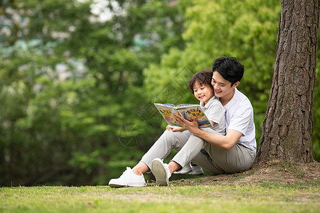 陪伴孩子父子在公园里看童话故事书背景