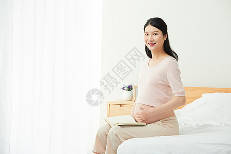 孕妇坐在床边阅读图片