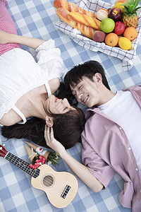 躺放的尤克里里青年情侣躺在野餐垫上背景