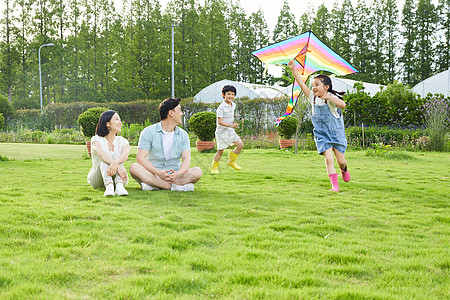 公园家庭年轻夫妻看着孩子追逐玩风筝背景