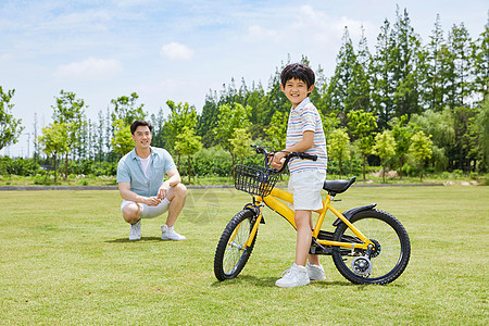 爸爸陪伴小男孩草坪上骑单车图片