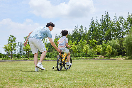 公园家庭爸爸陪伴小男孩骑自行车背影背景