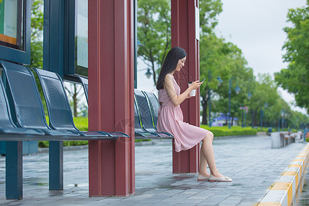 坐在公交站台玩手机的女性图片