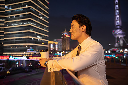 夜晚都市天桥上的商务男性手捧咖啡图片