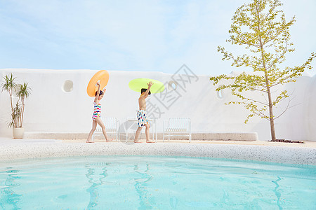 小女孩和夏天小男孩和小女孩拿着游泳圈在泳池边行走背景