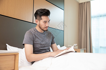 男性出差躺在酒店床上看书高清图片